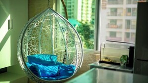 Ein Hängestuhl mit blauer Sitzkissen in einem Zimmer mit Fenster und Blick auf Gebäude.