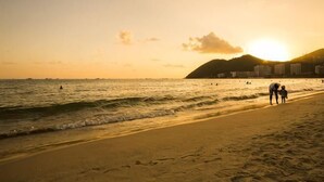 Eine Strandansicht mit Sonnenuntergang, Meereswellen und ein paar Personen, die am Ufer entlanggehen.