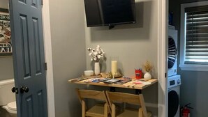 Une petite buanderie équipée d’un lave-linge, d’un sèche-linge, d’un extincteur et d’une table sur laquelle est posé un vase de fleurs.