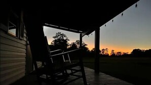 Une véranda avec un banc en bois, une vue sur le coucher de soleil et un champ verdoyant.
