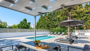 Ein Außenpoolbereich mit Liegestühlen, einem Tisch mit Früchten und Getränken sowie einer Pergola mit Dach.