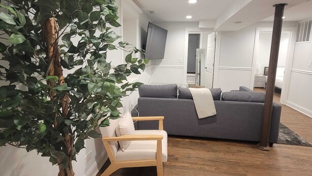 A modern living room with a grey sofa, a wooden chair, and a large artificial tree. - Cozy 2-bedroom apartment in welcoming Chicago in the Wicker Park area (Chicago)