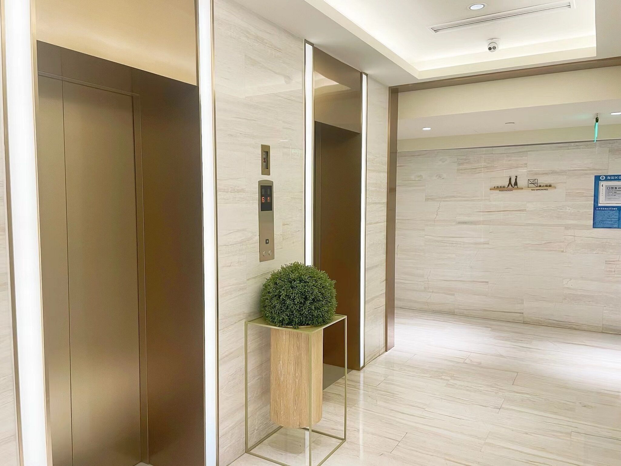 A modern elevator with a digital display, a small potted plant, and a sign indicating no smoking.