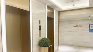 A modern elevator with a digital display, a small potted plant, and a sign indicating no smoking. - Ji Hotel (Beijing)