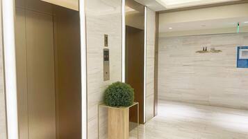 A modern elevator with a digital display, a small potted plant, and a sign indicating no smoking.