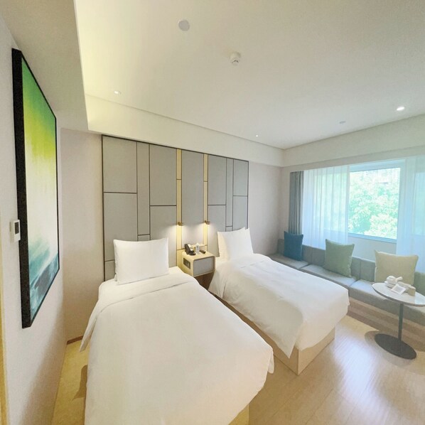 Une chambre d’hôtel avec deux lits, une petite table, une table de chevet, une grande fenêtre avec des rideaux et un tableau au mur.
