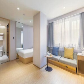 A modern hotel room with a sofa, a small table, a mirror, and a window with curtains. - Ji Hotel (Beijing)