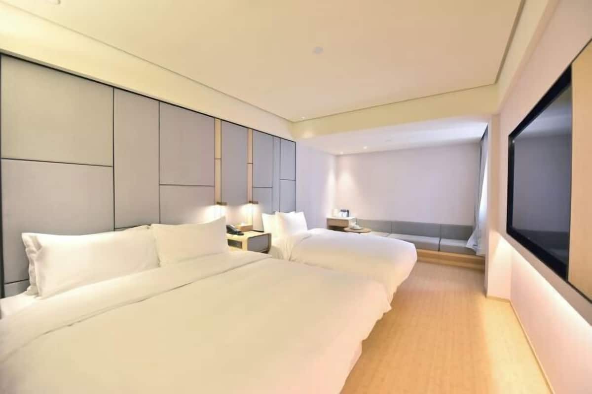 A hotel room with two beds, a large flat-screen TV, and a view of the city.