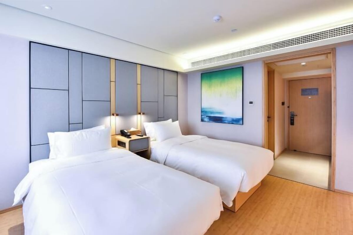 A hotel room with two beds, a nightstand, a painting, and a wooden door.