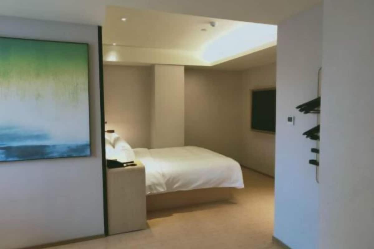A modern bedroom with a bed, a nightstand, a painting, and a wall-mounted TV.
