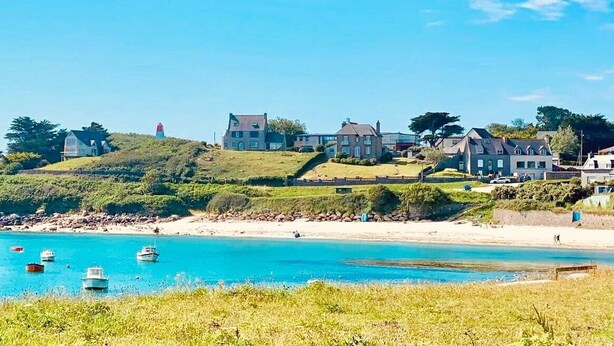 Blick auf die Küste mit Häusern an einem Hügel, einem Sandstrand und Booten im Wasser.
