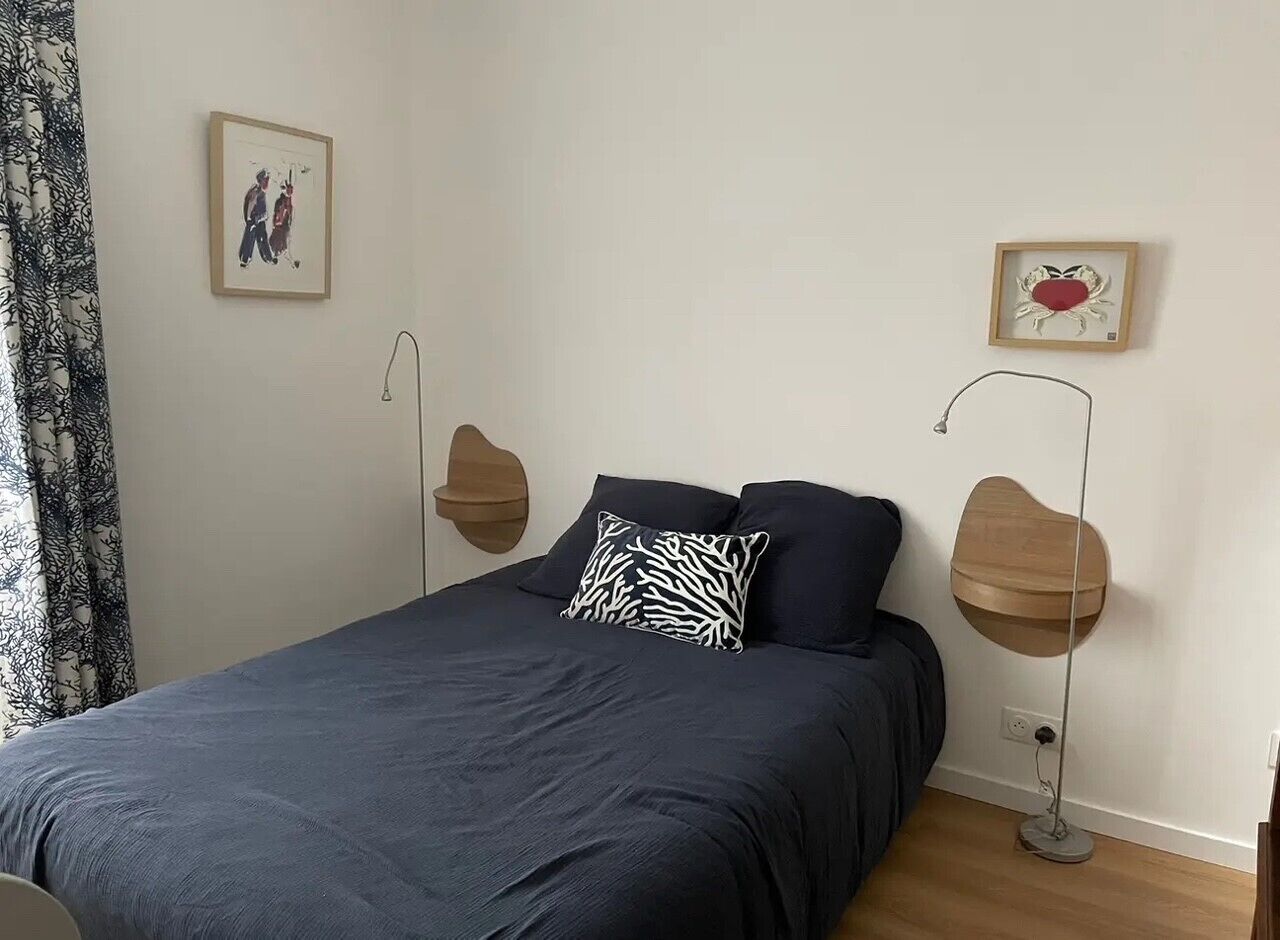 A bedroom with a bed, two wall-mounted lamps, and two framed pictures.
