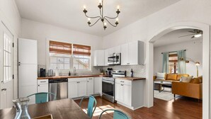 A modern kitchen with white cabinets, a wooden dining table, and teal chairs.