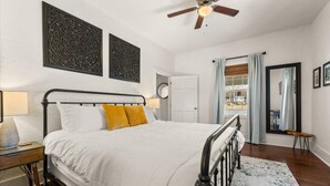 A bedroom with a bed, a nightstand, a lamp, a ceiling fan, and a view of the outdoors.