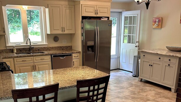 Una cocina con una isla central, sillas de madera, un refrigerador de acero inoxidable y una lámpara colgante.