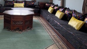 Une pièce comprenant un grand canapé, une table ronde en bois, des tapis à motifs et un plafond décoratif.