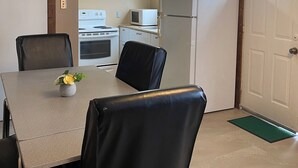 A compact kitchen with white cabinets, a refrigerator, and a dining area with a table and chairs. - 3-bedroom Wasaga Beach Walk to beach Free Parking Free Wifi (Wasaga Beach)