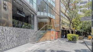A modern building with a glass facade, a staircase leading to an entrance, and outdoor seating area. - Icon Cibeles heart of La Roma (Mexico City)