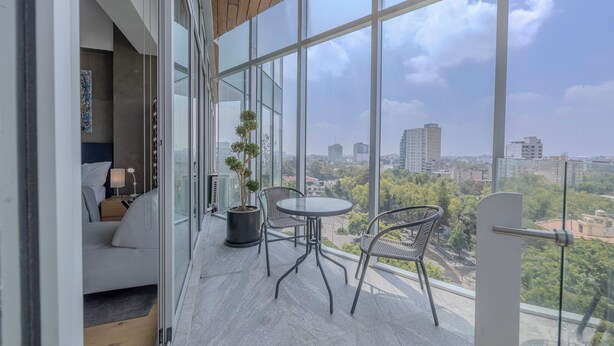 A balcony with a glass door, a small round table, two chairs, and a potted plant. - Icon Cibeles heart of La Roma (Mexico City)
