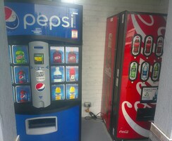 Dos máquinas expendedoras, una con Pepsi y la otra con Coca-Cola, frente a una pared lisa.