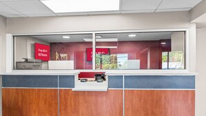 A reception desk with a glass partition, a red sign indicating free Wi-Fi, and a view of the outside. - HomeTowne Studios by Red Roof Richmond - Airport/Sandston (Sandston)