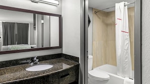 A modern bathroom with a granite countertop sink, a mirror, a shower with a white curtain, and a toilet. - HomeTowne Studios by Red Roof Richmond - Airport/Sandston (Sandston)