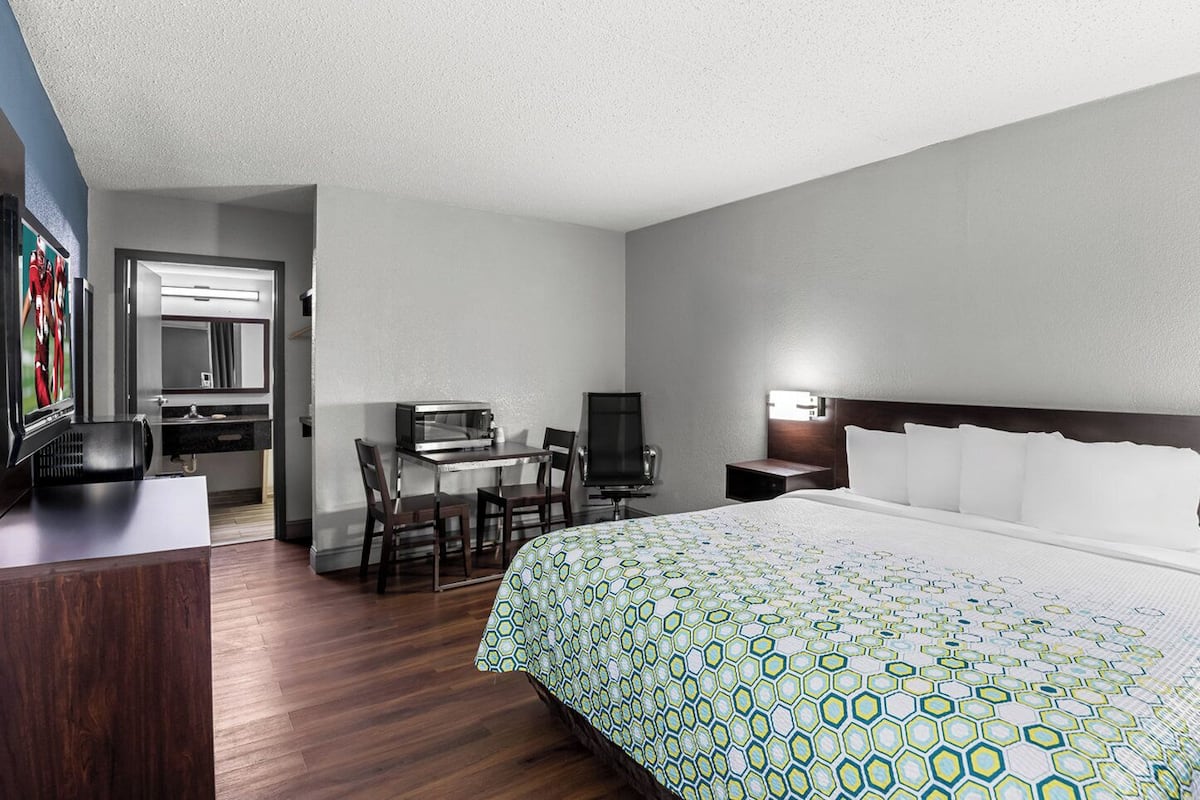 Habitación de hotel con cama, escritorio con computadora, televisor y baño con espejo y lavamanos.