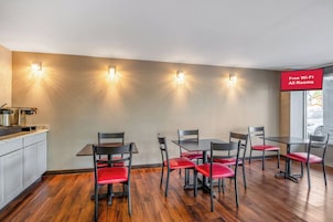 Un comedor con mostrador de cocina, cuatro mesas y sillas con cojines rojos.