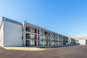 A multi-story motel with a row of balconies, a parking lot, and a clear blue sky. - HomeTowne Studios by Red Roof Richmond - Airport/Sandston (Sandston)