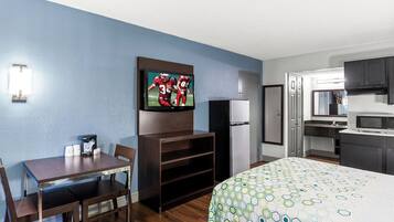 A hotel room with a bed, a TV mounted on the wall, a refrigerator, a microwave, a sink, and a dining table with chairs.