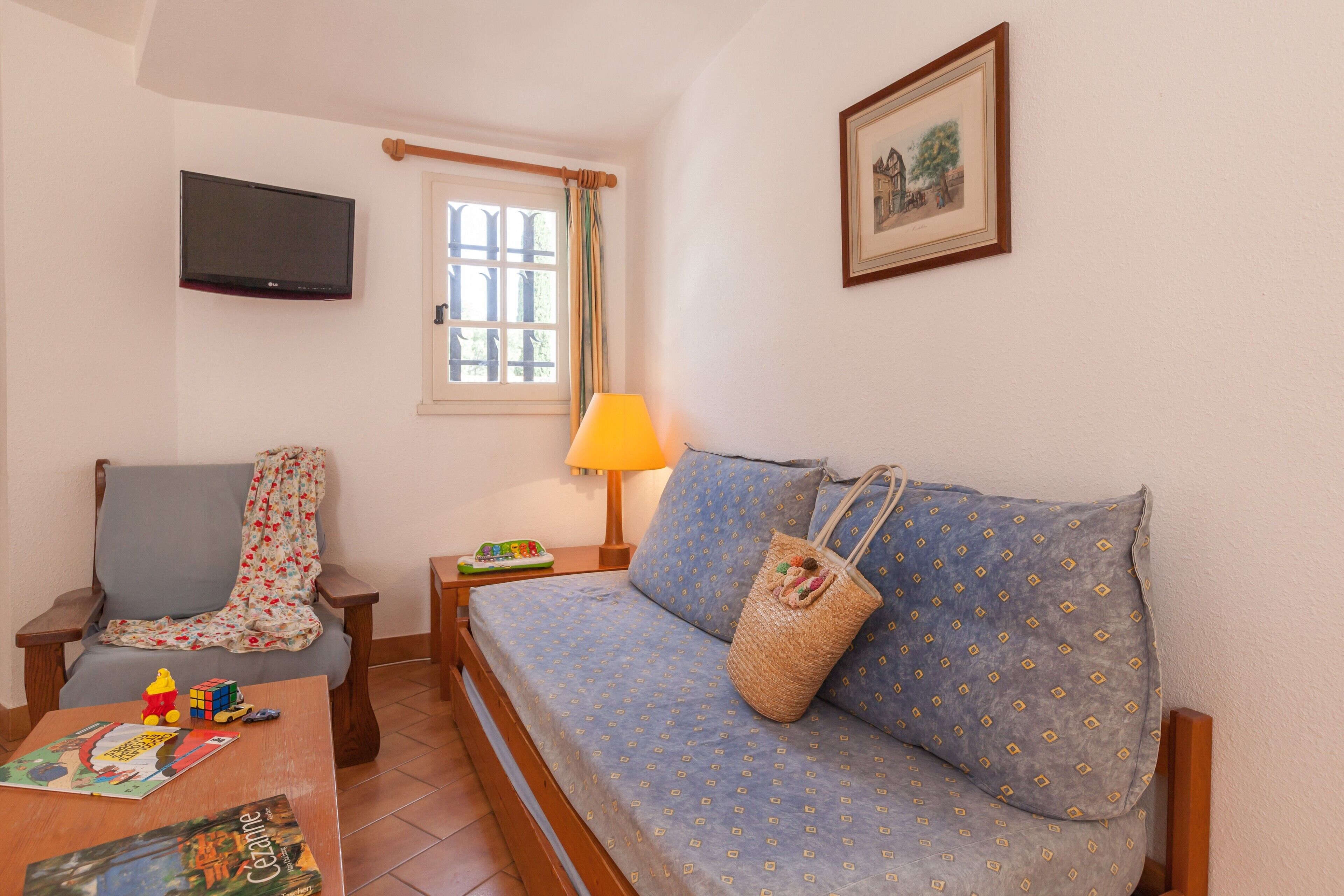 A cozy room with a sofa, a chair, a TV mounted on the wall, a window with curtains, and a lamp on a side table.