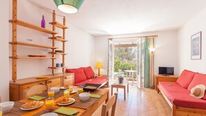 A bright room with a wooden dining table, breakfast setup, and a cozy seating area with a red sofa and a TV. - Résidence Le Domaine de Garlande (Cavalaire-sur-Mer)
