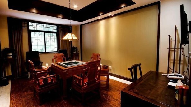 Un comedor con una mesa y sillas de madera, una lámpara colgante y un ventanal con un diseño geométrico.