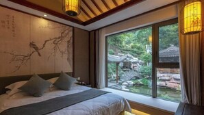 A bedroom with a large bed, a view of a garden, and traditional decor.