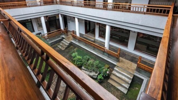 A multi-level atrium with wooden railings, stone flooring, and potted plants.