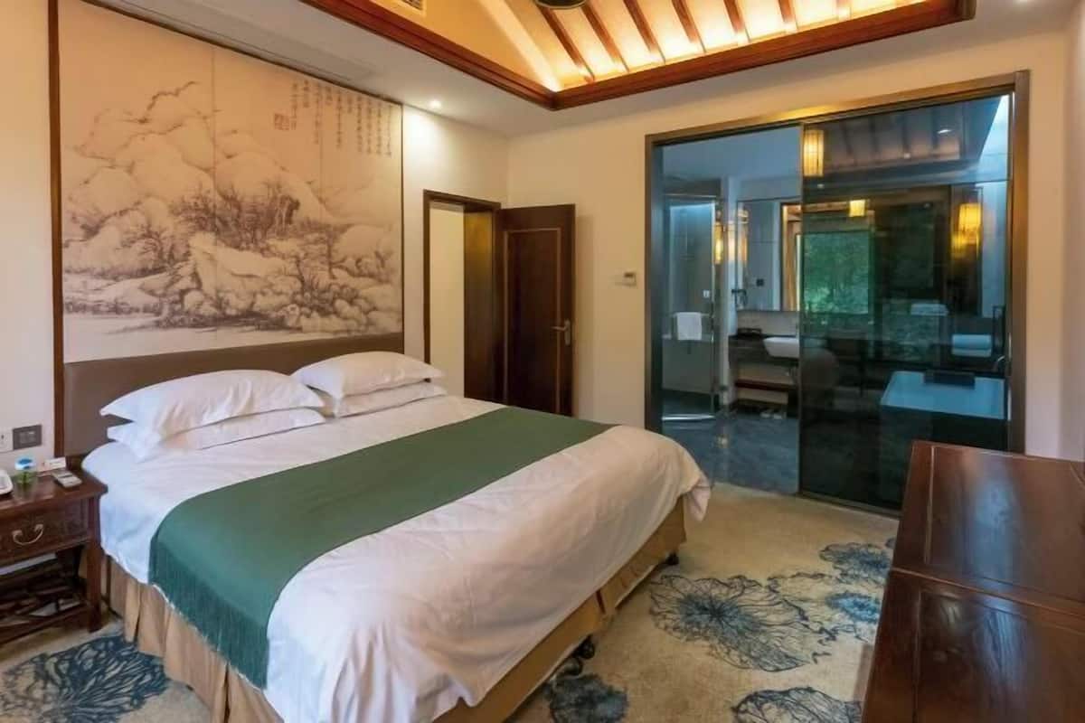 Une chambre d’hôtel comprenant un lit, une table de chevet, un mur décoré d’œuvres d’art, une porte et une porte vitrée donnant sur une salle de bain.