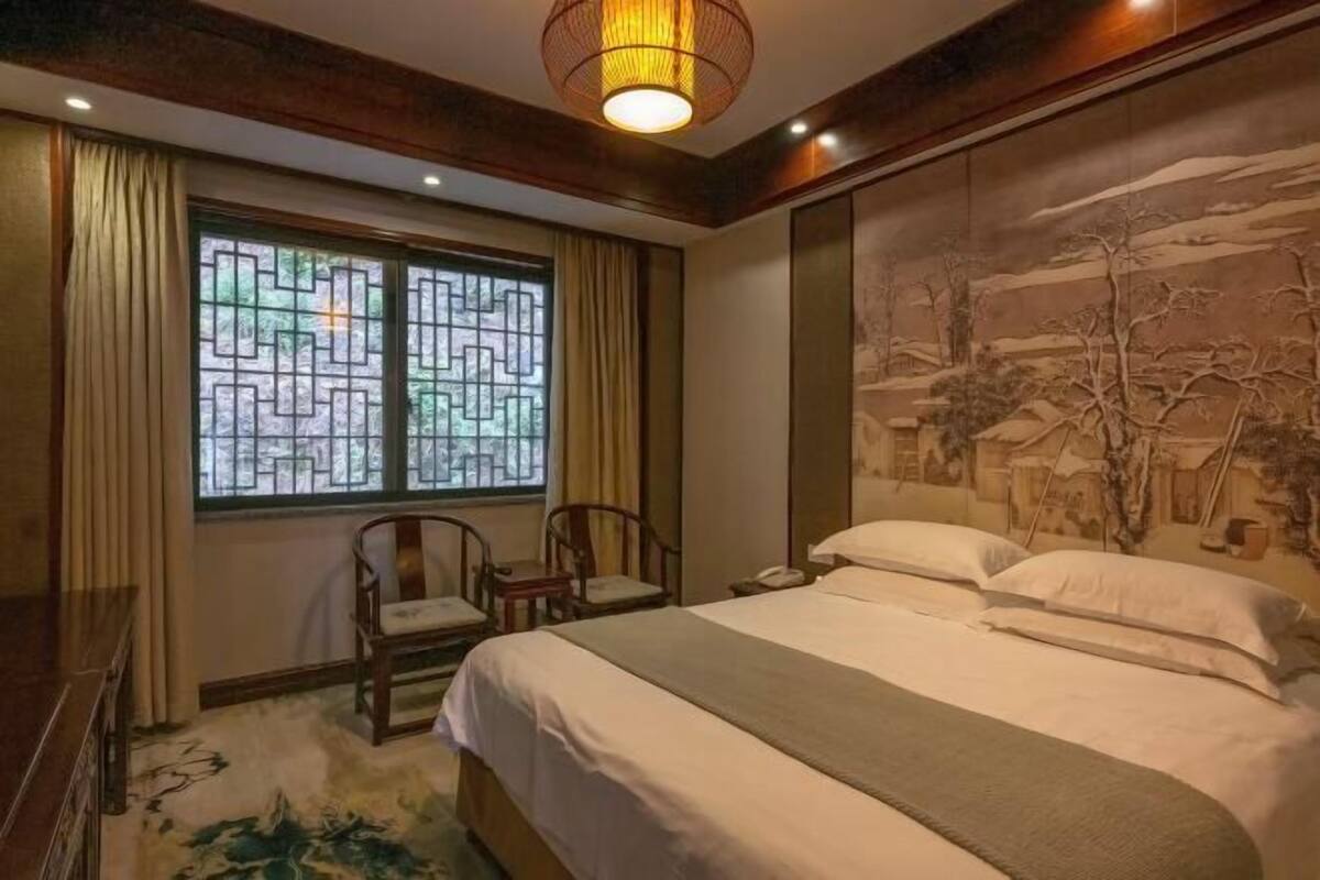 Une chambre d’hôtel avec un lit, deux chaises, une fenêtre ornée d’un motif géométrique et une fresque murale.