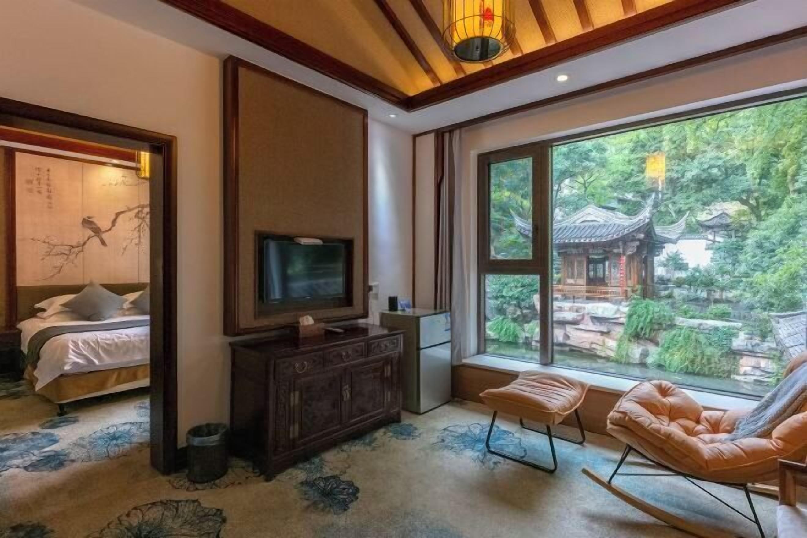 A room with a bed, a TV, a dresser, a window with a view of traditional architecture, and a seating area.