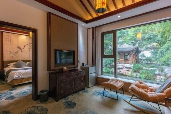 A room with a bed, a TV, a dresser, a window with a view of traditional architecture, and a seating area. - Wuyi Yangchun Shanju Guesthouse (Wuyi)