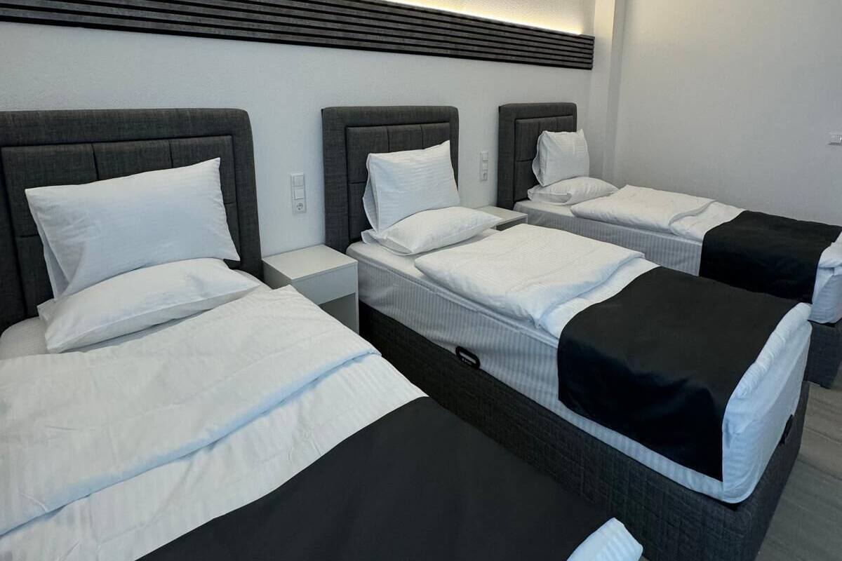 Een hotelkamer met drie bedden op een rij, elk met een donker hoofdeinde en wit beddegoed.