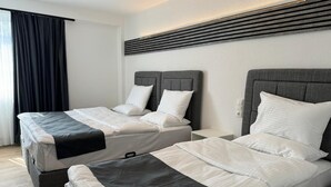 A hotel room with two beds, each with a grey headboard, white bedding, and a black accent. - Dido Diamond Hotel (Dietzenbach)