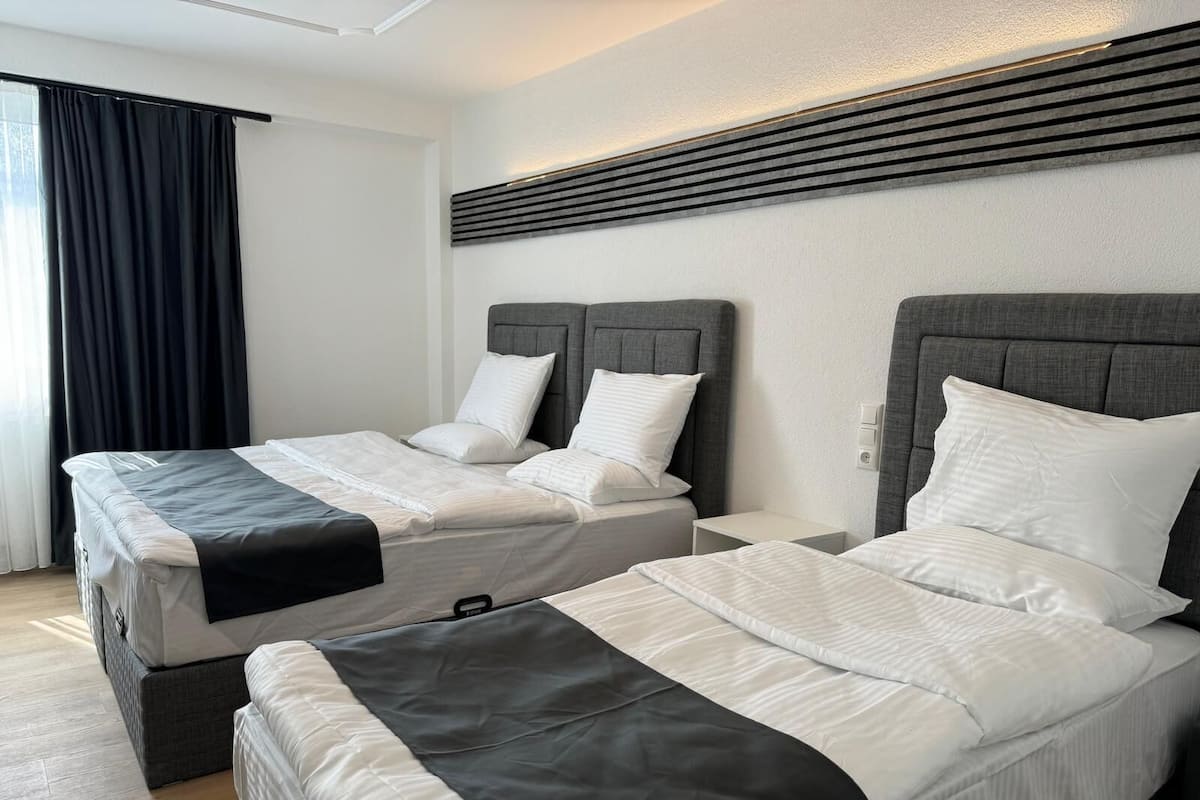 Een hotelkamer met twee bedden, elk met een grijze hoofdbord, witte beddengoed en een zwarte accent.
