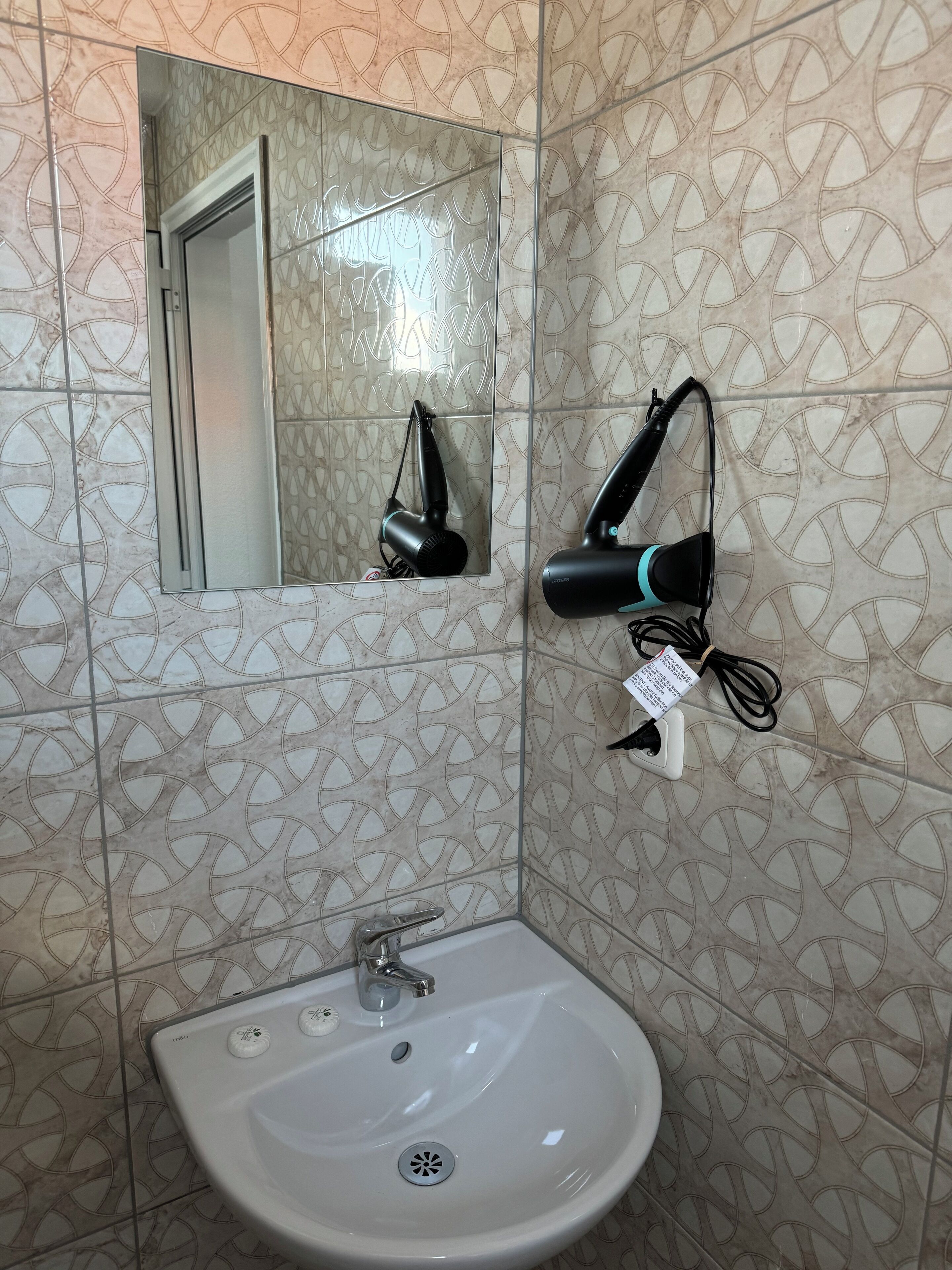 A bathroom with a sink, mirror, and two hair dryers mounted on the wall.