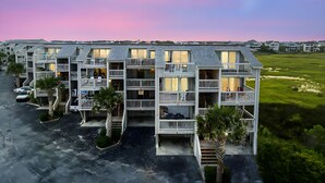 Un edificio residencial de varios pisos con balcones, zona de estacionamiento y paisaje con césped.