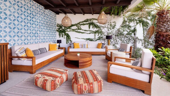 A cozy outdoor seating area with a round wooden coffee table, cushioned sofas, and patterned ottomans.
