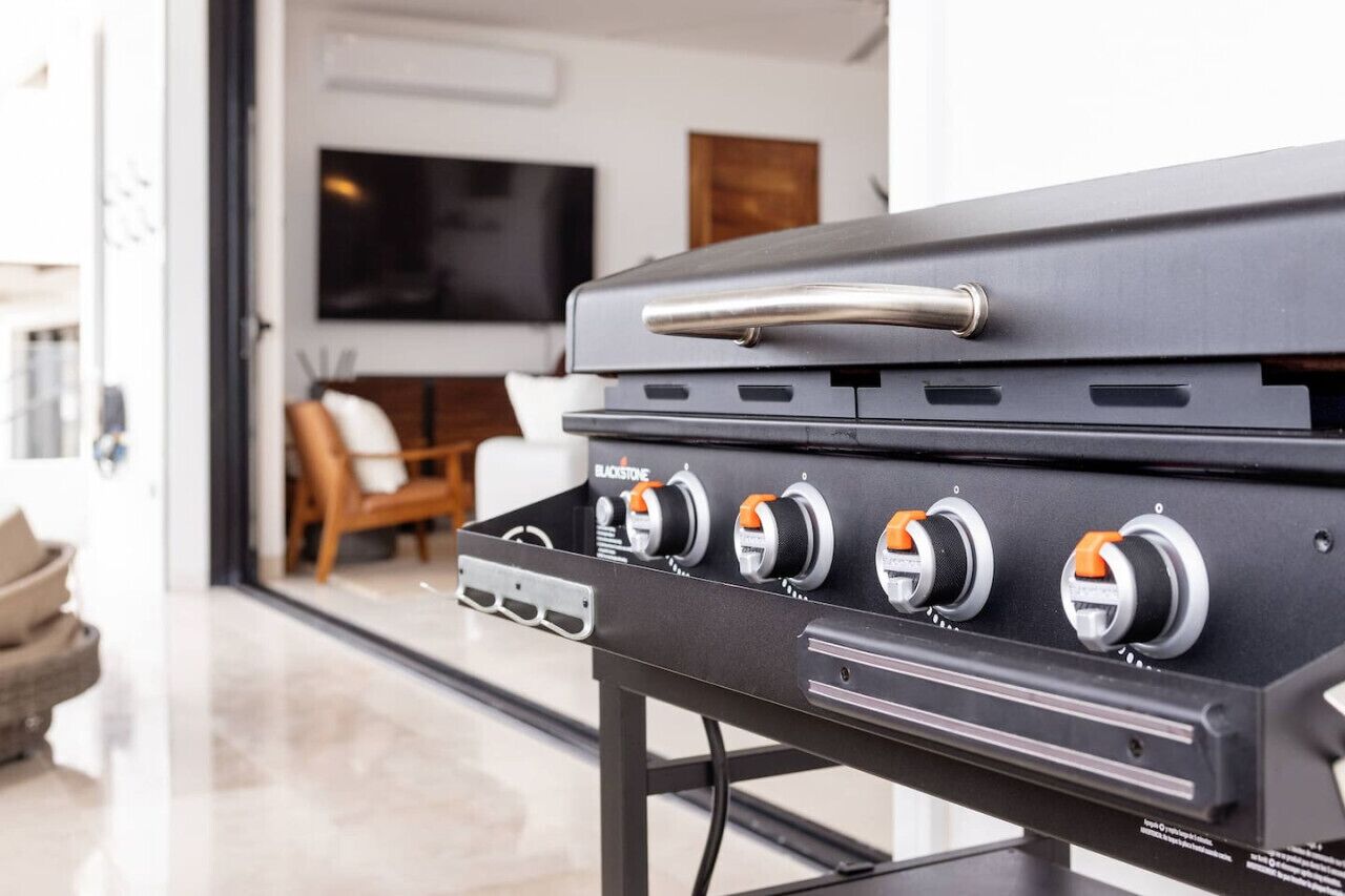 A modern kitchen with a built-in grill station featuring four burners and a stainless steel handle.