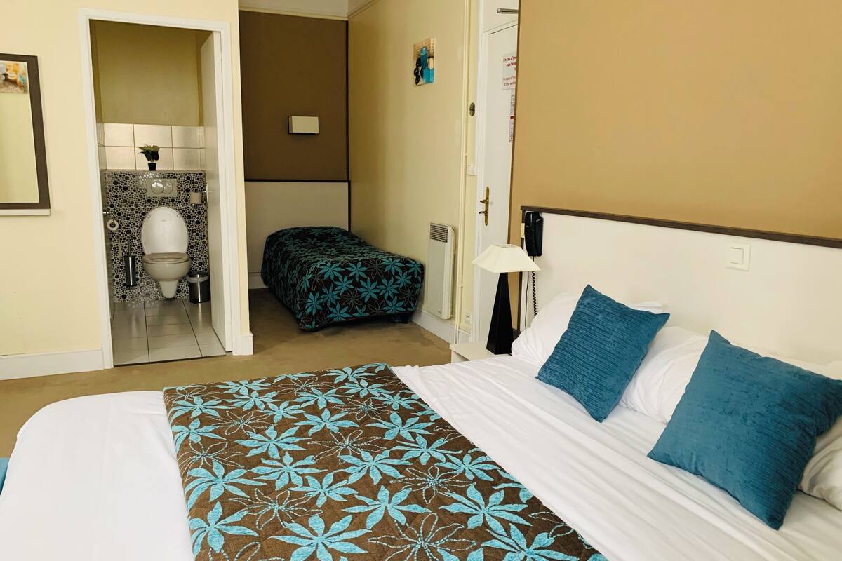 A hotel room with a bed, a bedside table with a lamp, a bathroom with a toilet and sink, and a door with a sign.