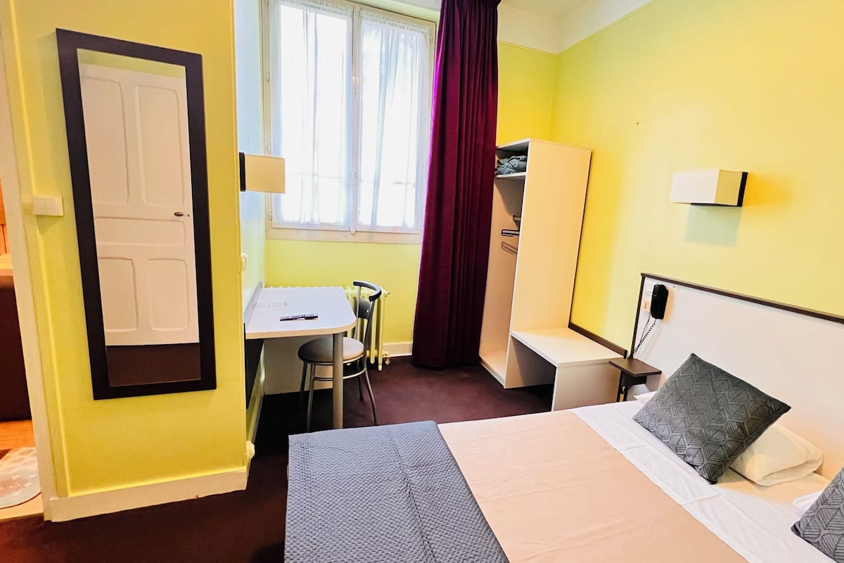 A hotel room with a bed, a desk, a chair, a wardrobe, and a window with curtains.