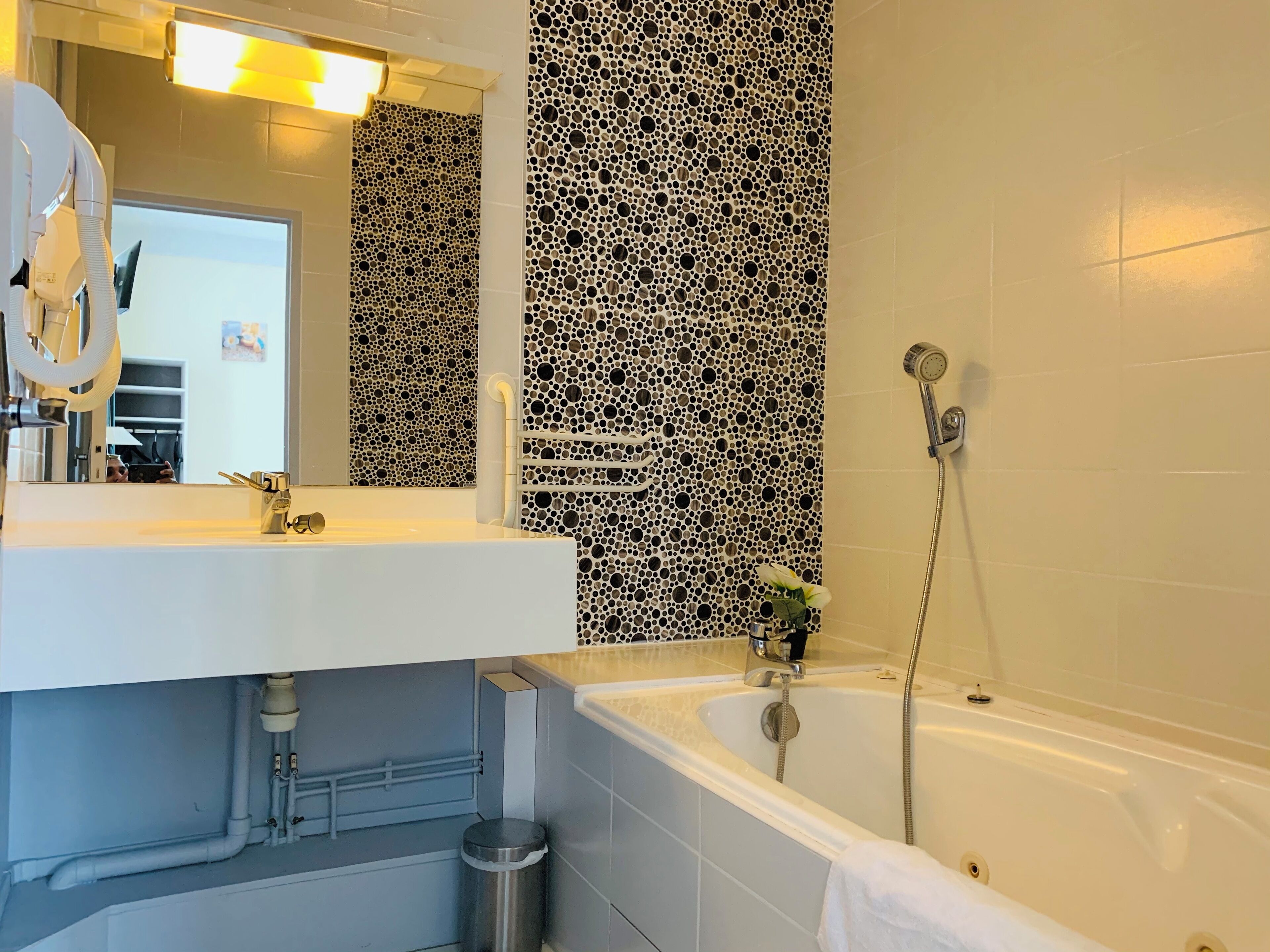 A modern bathroom with a white sink, a mirror, a shower, and a patterned wall.