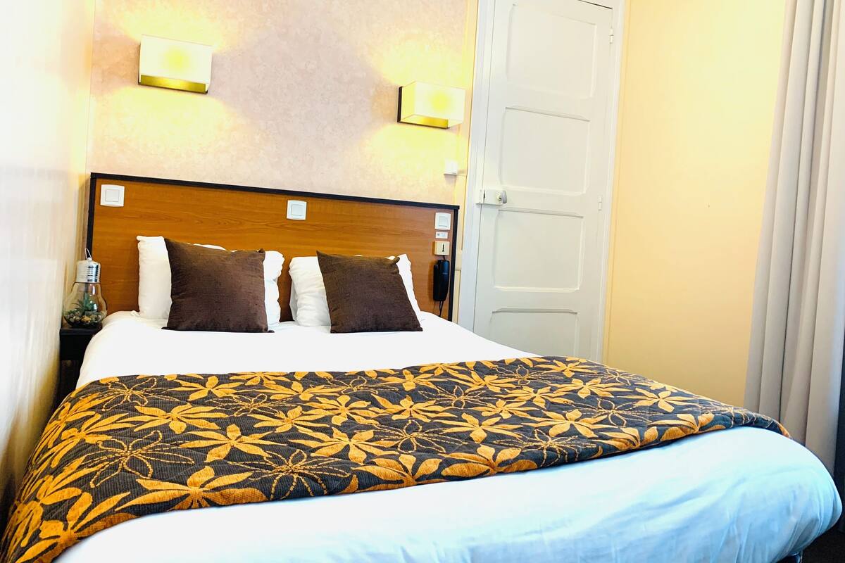 A hotel room with a bed, a nightstand, a lamp, and a door.